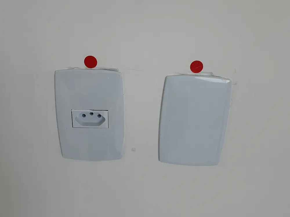 Tomada e interruptor sinalizados em vistoria, com espelhos desalinhados